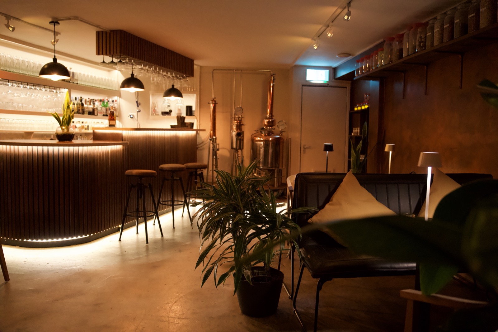 The Distillery interior — lit bar counter, copper still, and lounge seating